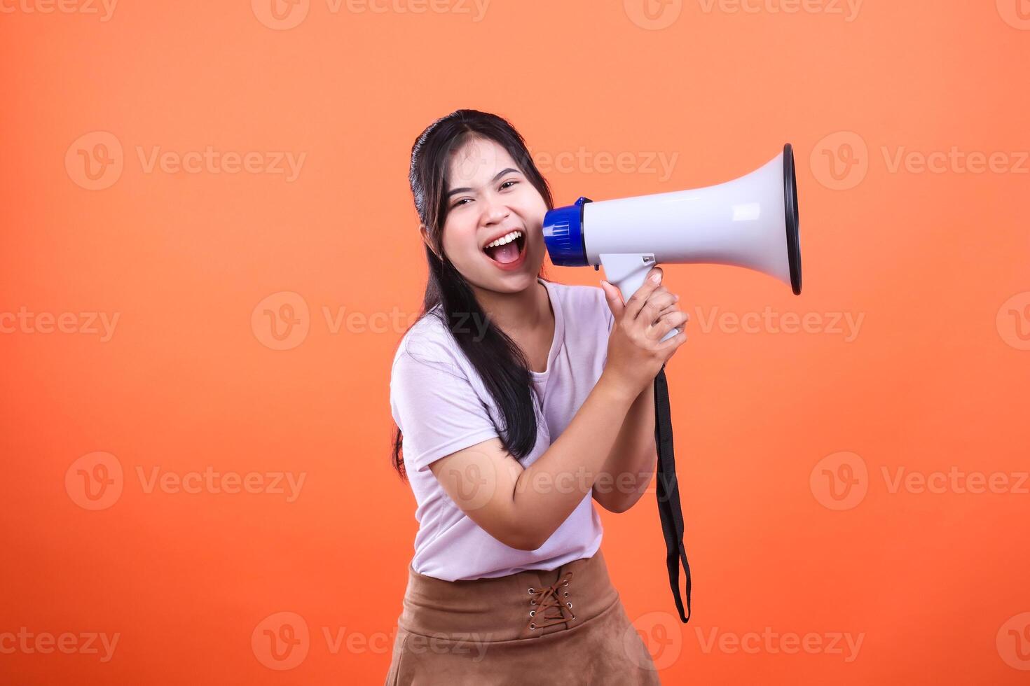 Enthusiastic woman using megaphone with an orange background announcing news photo