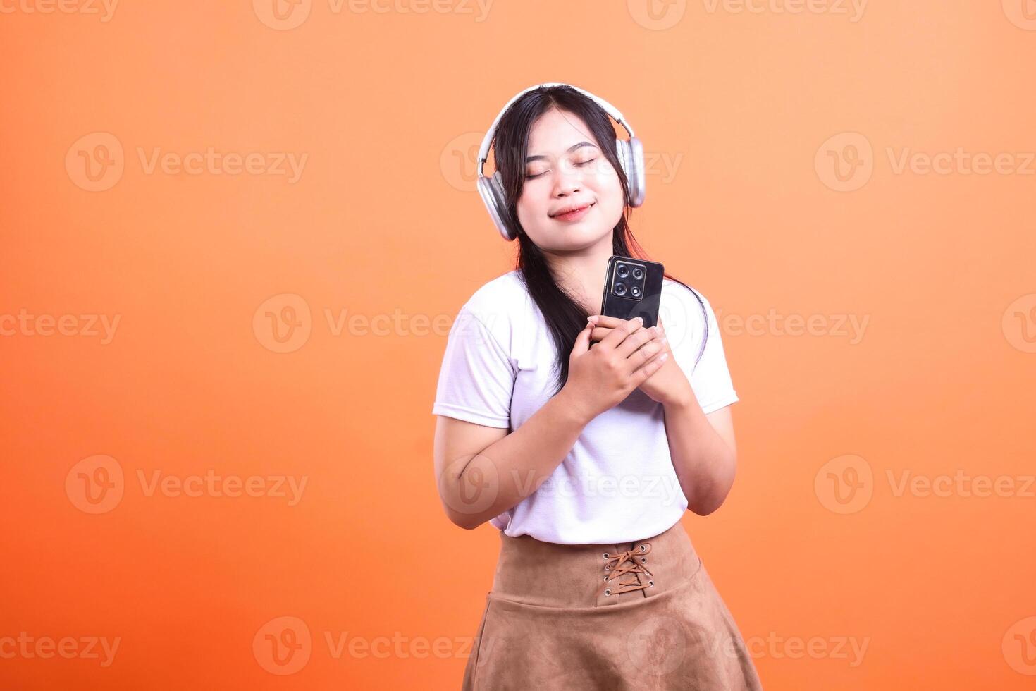 Young woman with headphones listening to music against an orange background photo