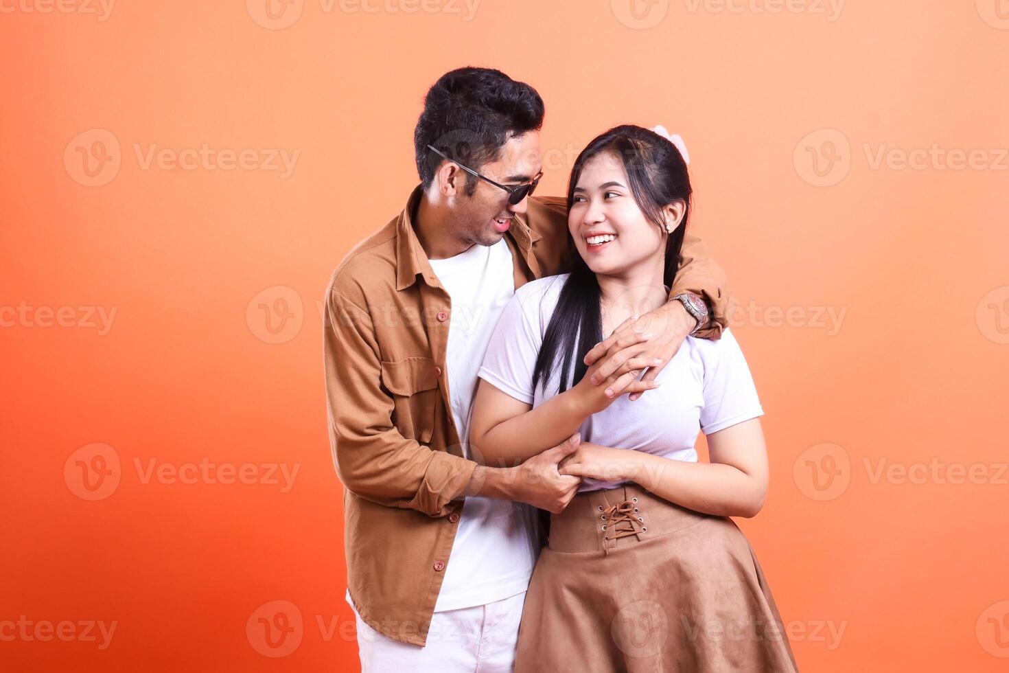 a couple of adult lovers happy expressions embracing and holding hands where the man is standing and the woman is looking at each other romantically. isolated on orange background photo