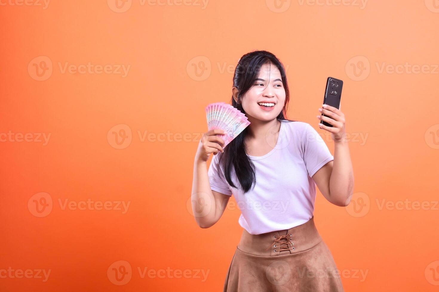A woman holding a fan of money and a mobile phone in her hands against an orange background photo