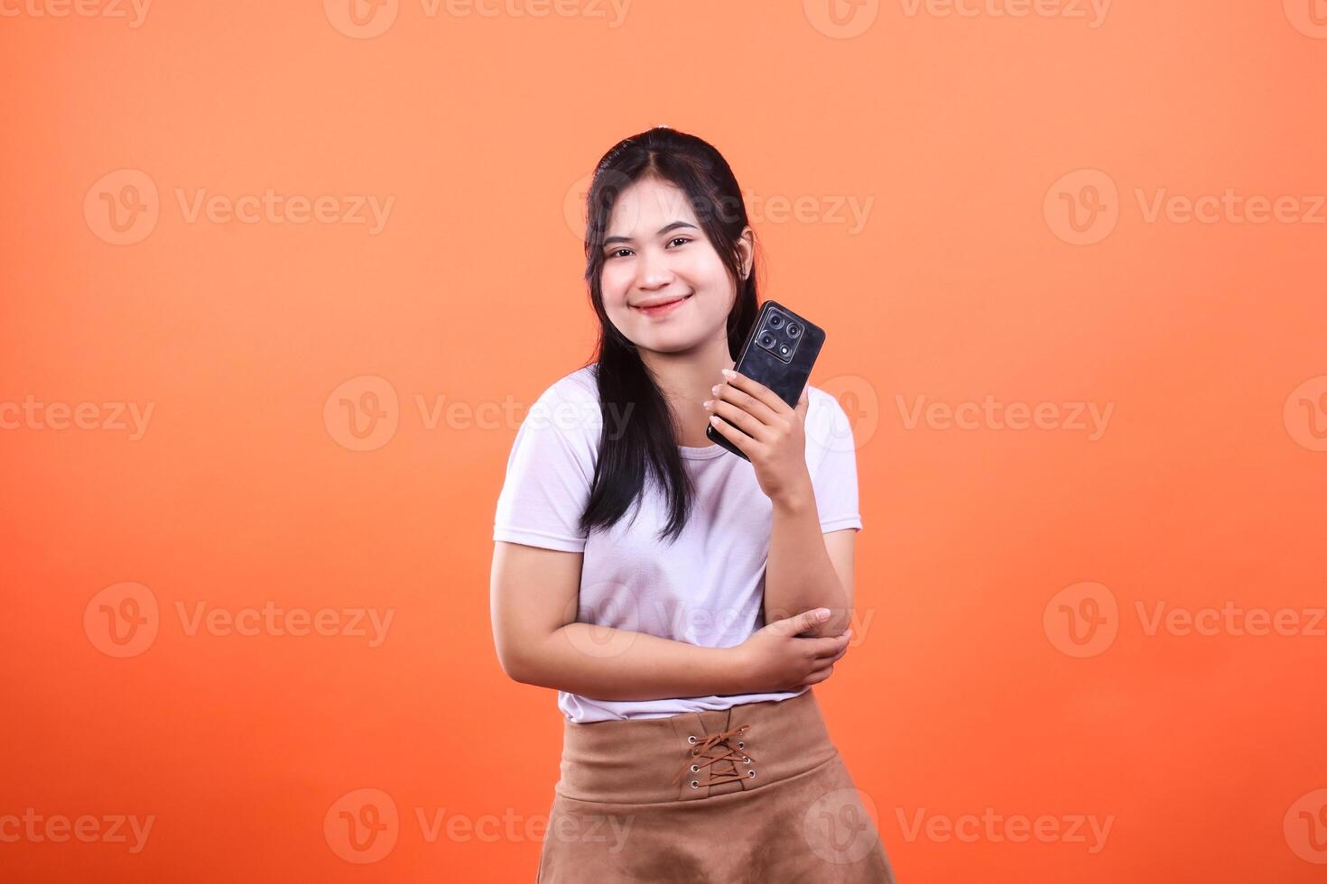 A woman holding a mobile phone with smile, standing on the orange background photo