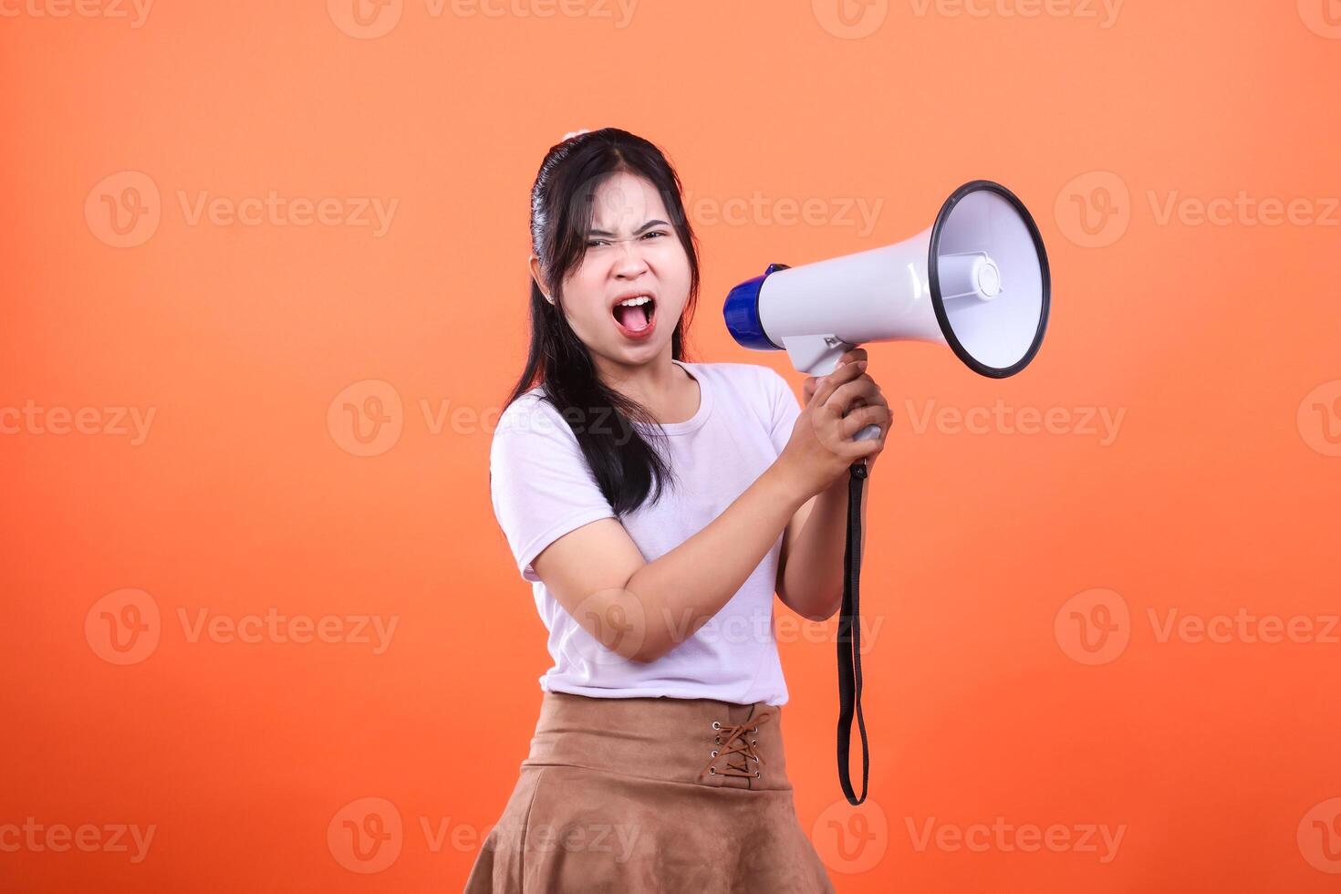 A person holds a megaphone in front of an orange background as she shouts loudly photo