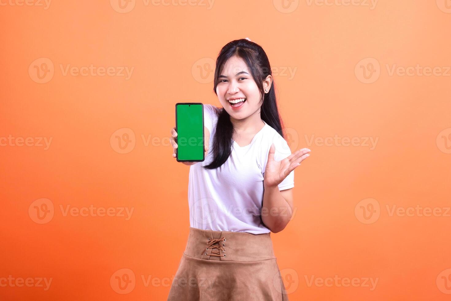 Smiling woman with long hair showing phone screen in front of orange background photo