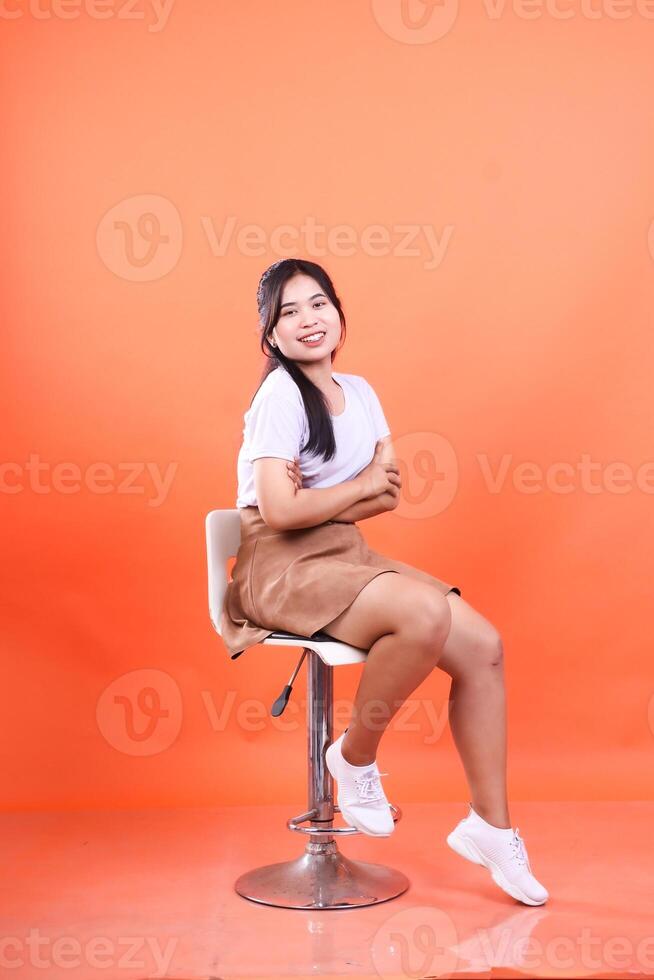 A Woman Posing on a Stool Isolated on a Vibrant Orange Background Studio Shot photo