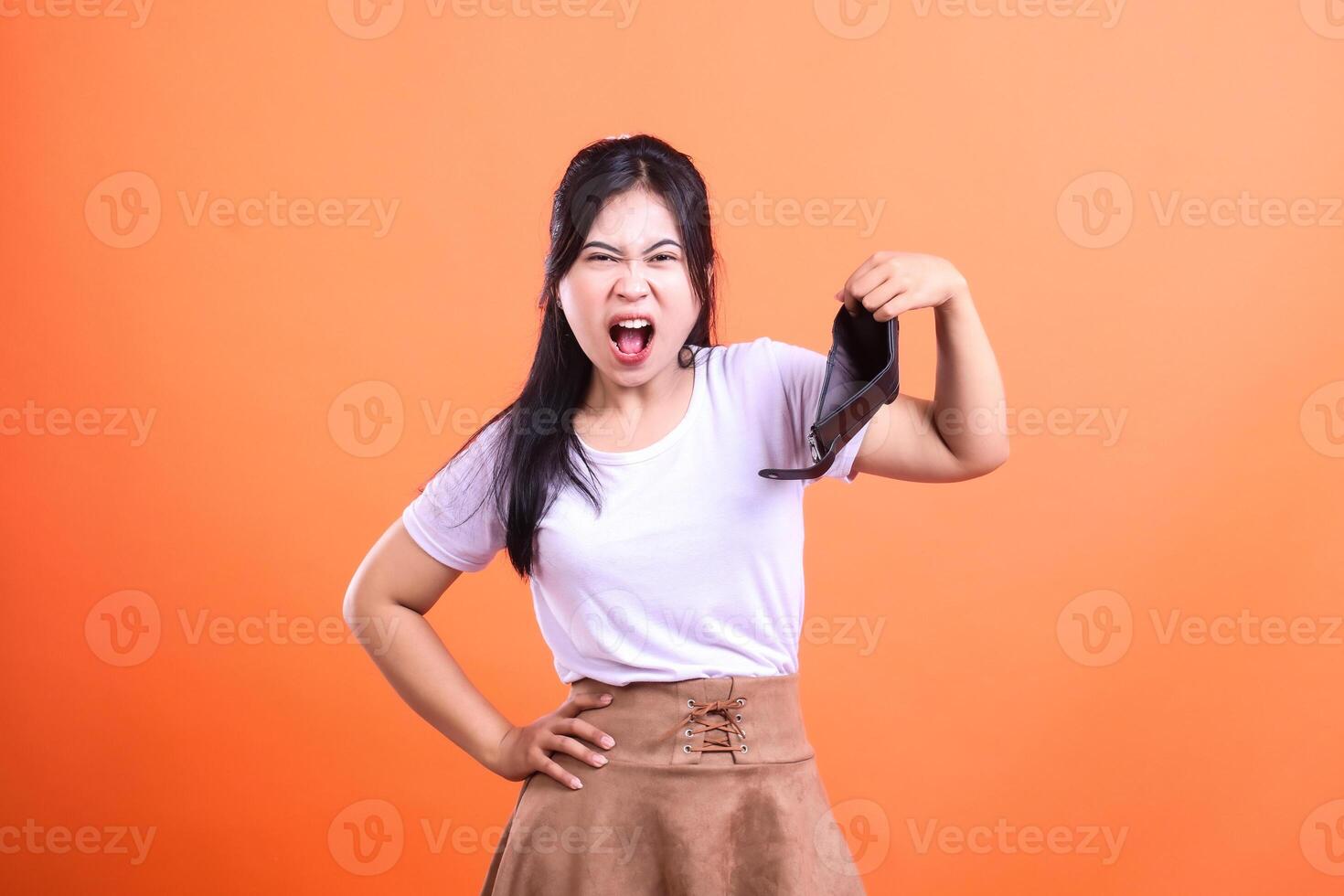A woman holding an empty wallet against an orange background expressing anger photo