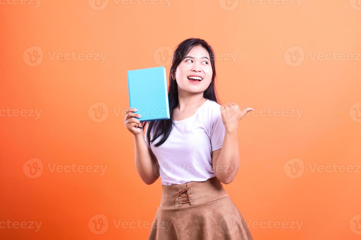 A person holding a blue book with their left hand and gesturing with their right on an orange background photo