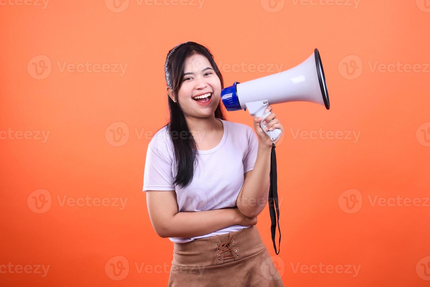 Woman smiling holding a megaphone in a bright orange background studio shot photo