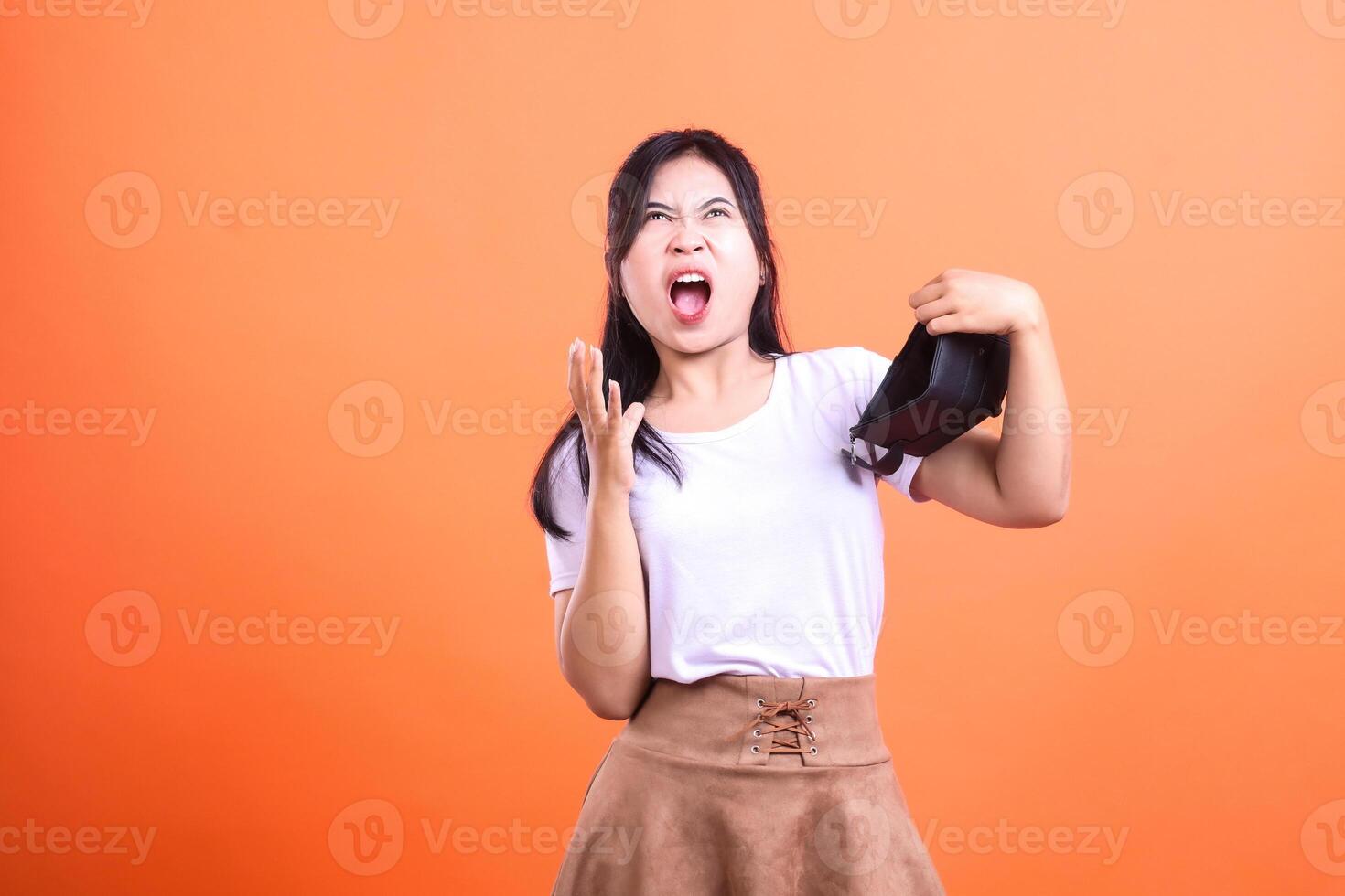 Woman holding an empty black bag with angry expression on orange background photo