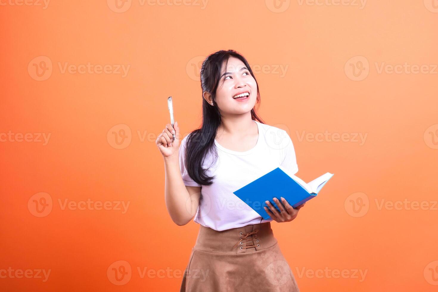 A person holding a blue book and a pen with a bright orange background looking up and smiling photo