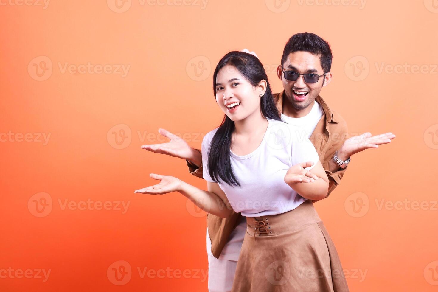 A smiling woman and a man with sunglasses are posing with open hands on orange background photo