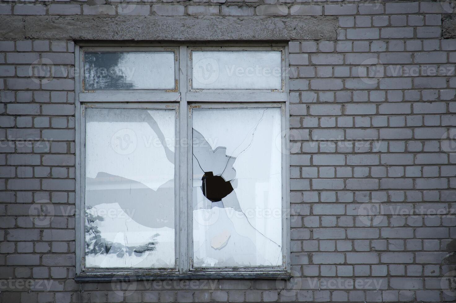 A broken window with shattered glass in an old brick wall evokes a sense of urban decay. photo