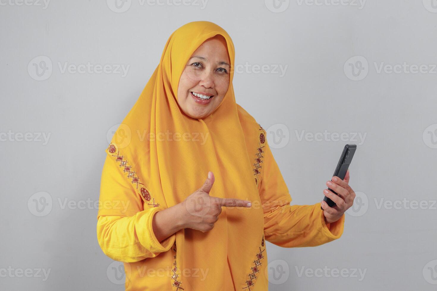 Smiling Muslim woman pointing at smartphone screen for app promotion photo