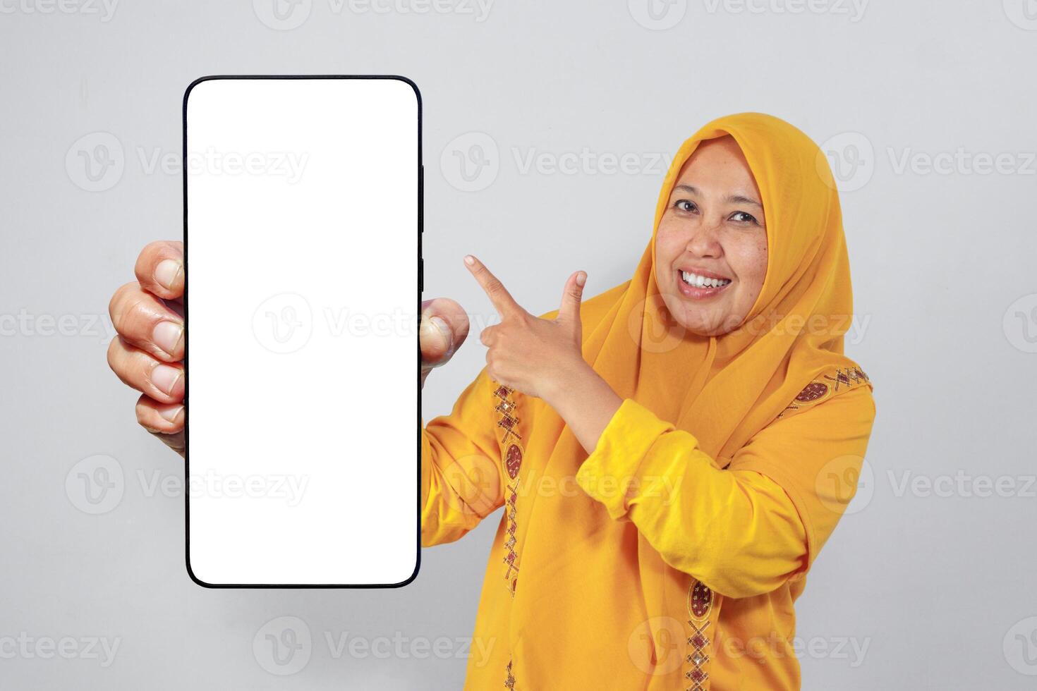 Happy woman in hijab showing and pointing at empty smartphone screen photo