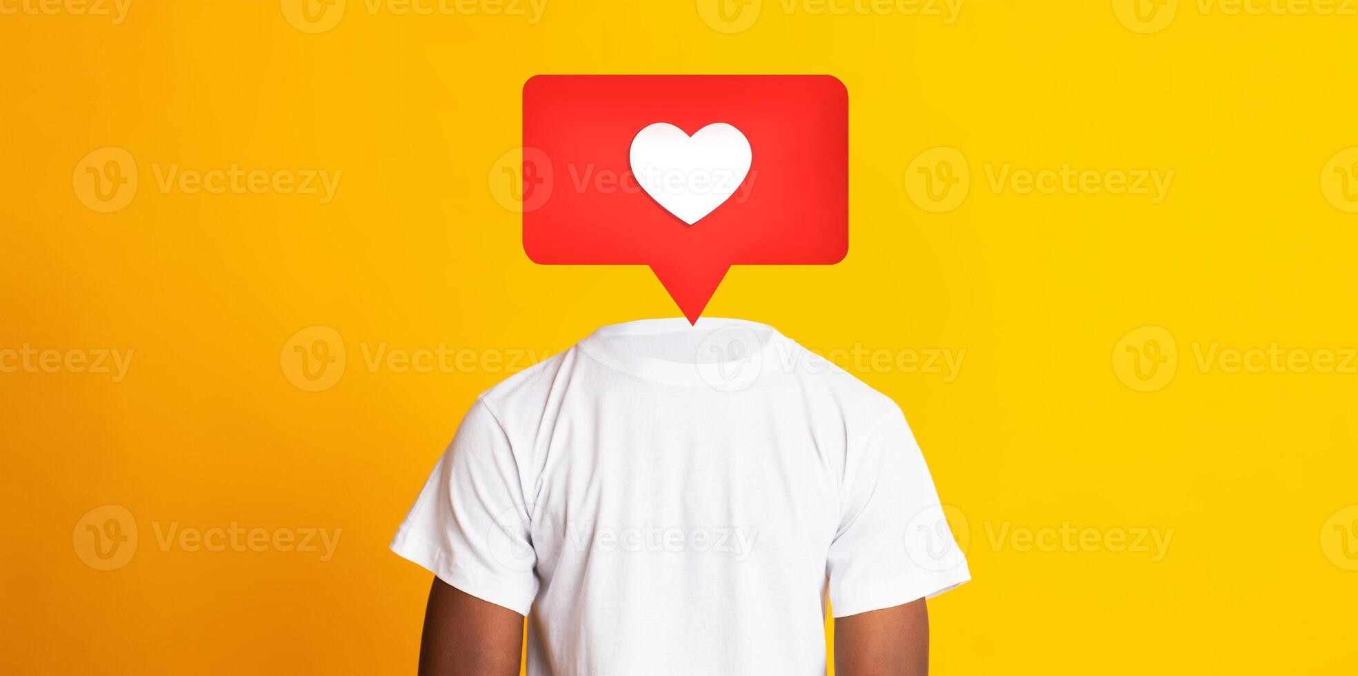 A person stands with their back turned, wearing a white t-shirt against a bright yellow background. A red heart icon appears instead of their head, symbolizing social media interactions. photo