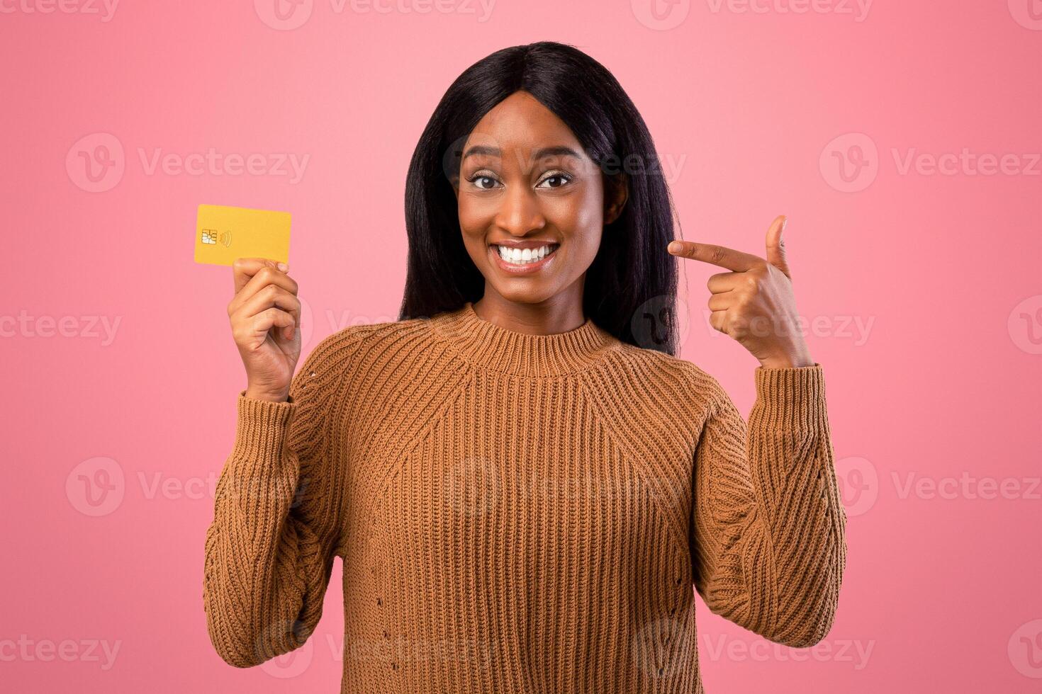 Easy shopping concept. Happy black woman pointing at credit card and smiling on pink studio background. Gorgeous African American lady promoting bank services, advertising online payments photo