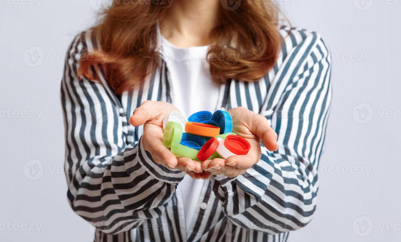 Lots Of Colorful Plastic Lids Bottle Caps In Hands Of Unrecognizable Lady. Eco-Friendly Woman Agitating For Zero Waste Living And Garbage Sorting, Standing On Grey Studio Background, Closeup Shot photo