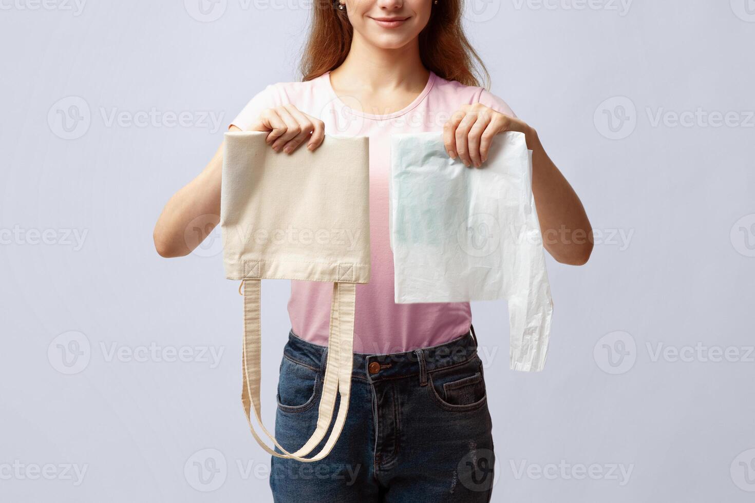 Zero Waste Shopping Concept. Unrecognizable Woman Holding Reusable Eco Bag In One Hand And Plastic Polyethylene Bag In Another While Standing Over Gray Studio Background, Cropped Image, Closeup photo