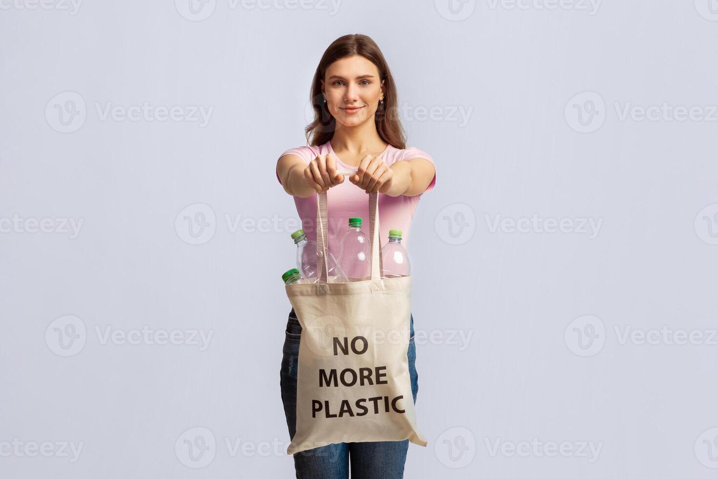 No More Plastic. Happy Young Lady Carrying Eco Tote Bag With Empty Bottles For Recycling, Smiling Nature-Lover Woman Promoting Zero-Waste Living, Posing Over Light Studio Background, Copy Space photo