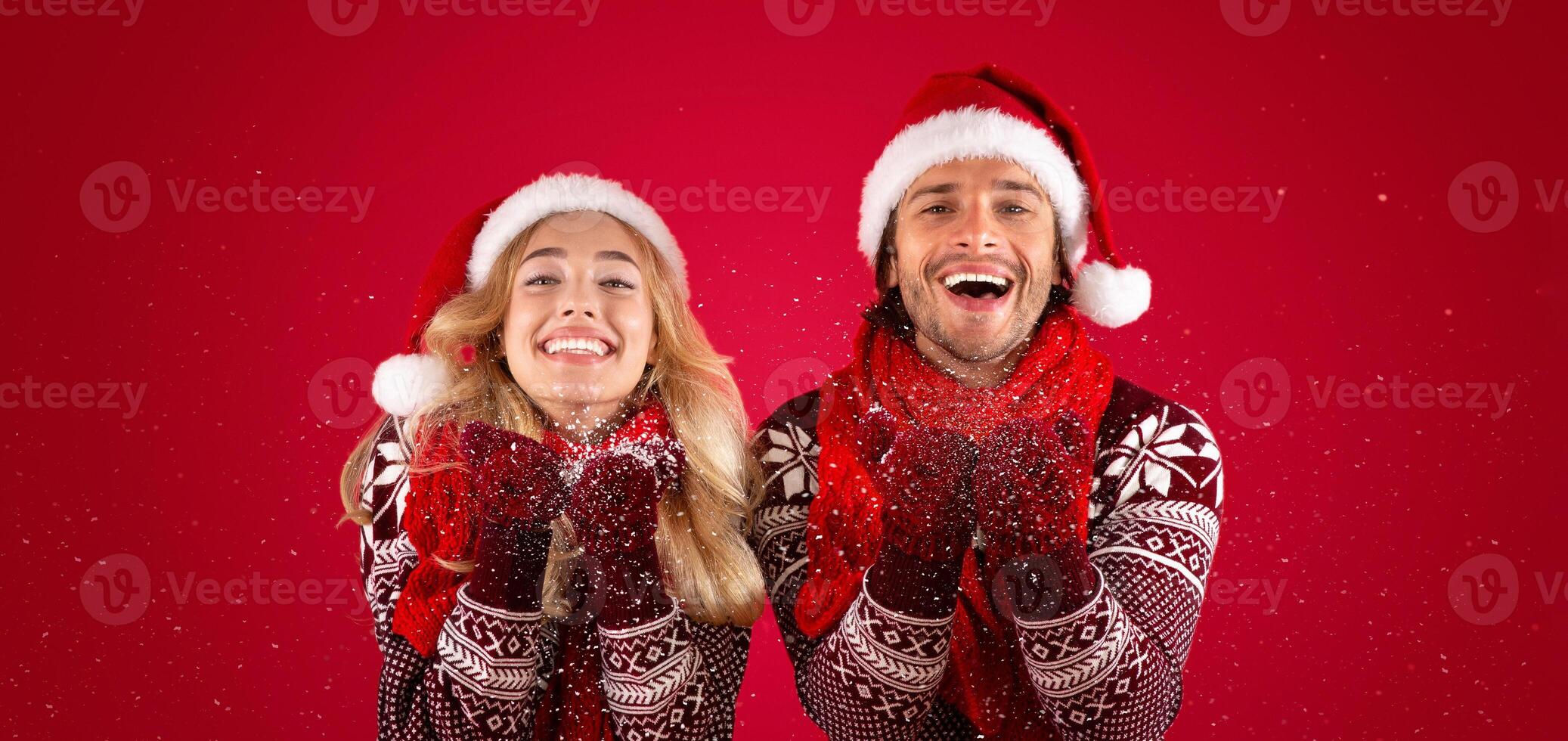 Christmas time. Happy millennial guy and his girlfriend blowing snow on red background photo