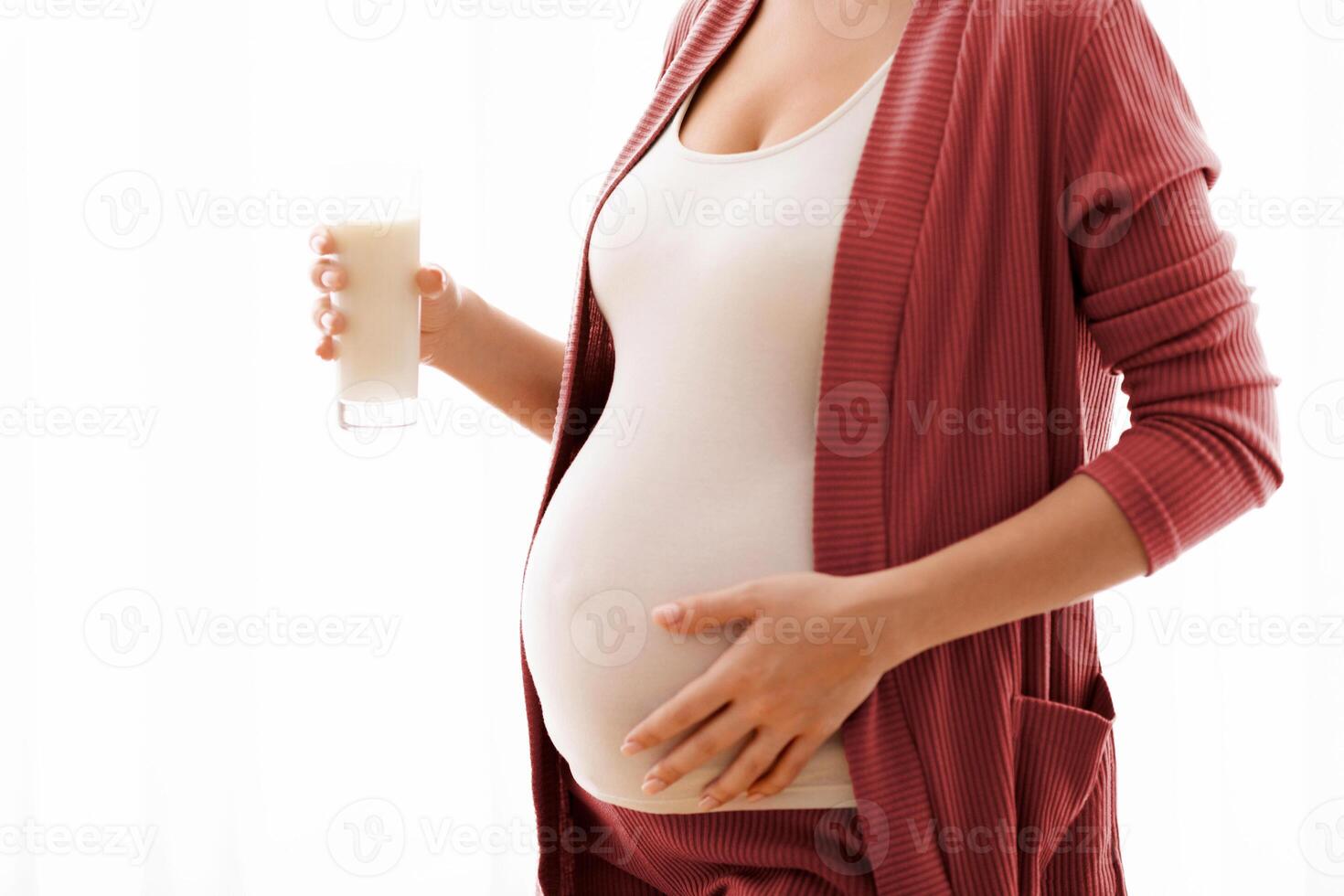 Unrecognizable Pregnant Woman With Glass Of Milk In Hands Standing Near Window And Touching Her Belly, Young Expectant Mother Enjoying Healthy Calcium Drink, Cropped Image With Copy Space photo