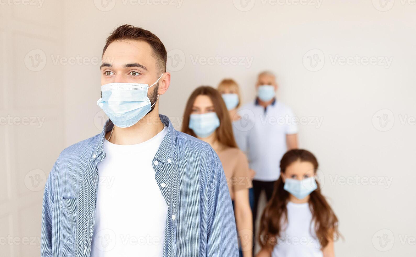 Young Caucasian guy in face mask waiting in line for coronavirus vaccination at health centre, copy space. Covid-19 immunization campaign, prevention of global virus concept photo