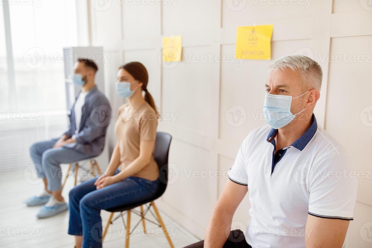 Covid-19 vaccination. Senior man in face mask waiting to receive coronavirus vaccine injection, sitting in queue at clinic, free space. Population immunization campaign, viral disease prevention photo