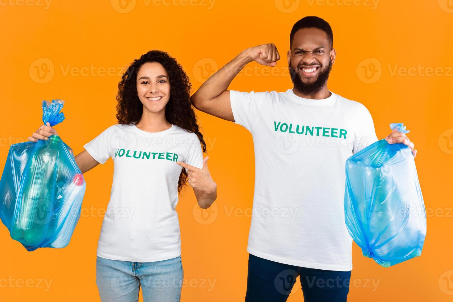 Volunteers Team. Multiracial Man And Woman Holding Blue Garbage Bags With Wasted Plastic Posing In Studio Over Yellow Background. Keep Environment Clean, Ecology And Volunteering Job photo