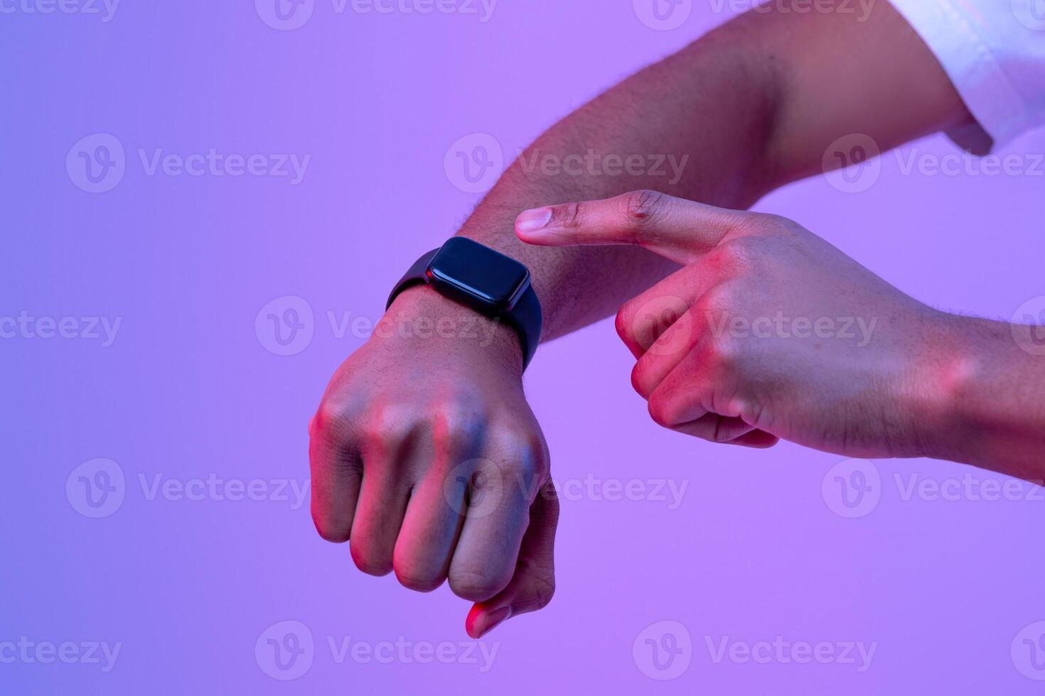 Smart devices. Unrecognizable african man pressing button on smart watch with black screen on his hand, standing in neon lighting over purple studio background, cropped image with free space, mockup photo