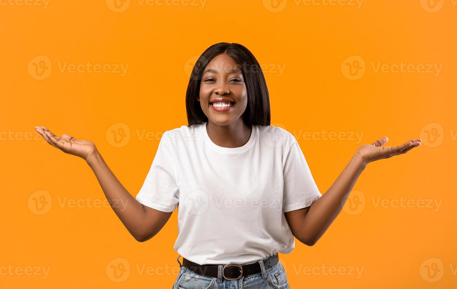Happy black lady raising hands up as holding something invisible on orange studio background, copy space. Smiling african american young woman showing or recommending something photo
