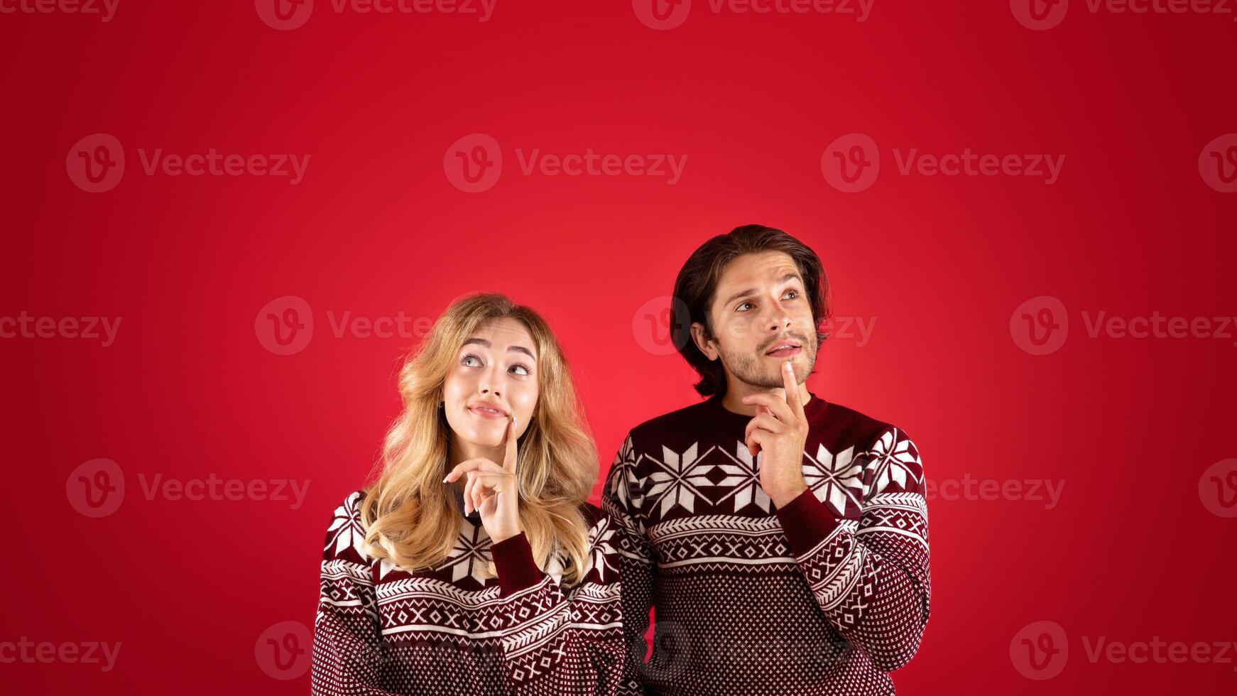 Thoughtful millennial couple in Christmas sweaters dreaming on red background photo