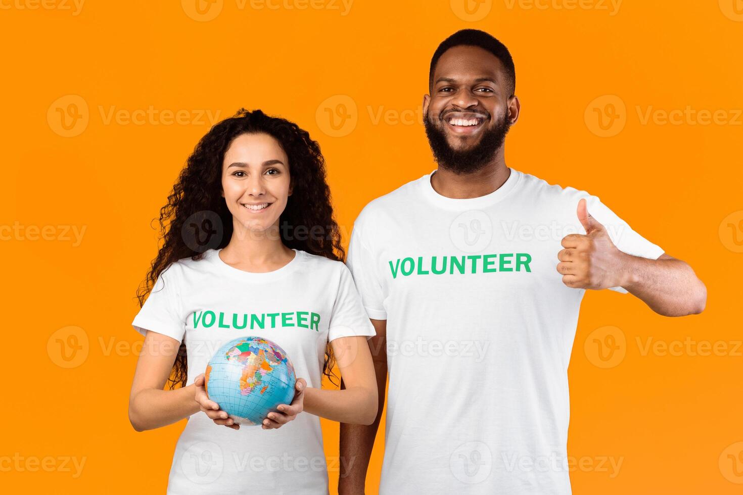 Two Diverse Volunteers Holding Earth Globe And Gesturing Thumbs Up Standing Posing Over Yellow Studio Background, Smiling To Camera. Ecology And Environment, Let's Protect Our Planet Concept photo