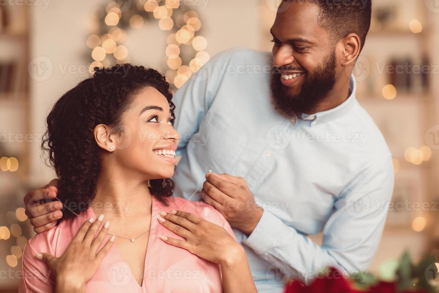Luxury Present. Smiling Black Young Lady Receiving Golden Pendant Necklace With Diamond For Holiday. Happy Lovely Couple Celebrating St Valentine's Day, Anniversary, Engagement Or Birthday photo