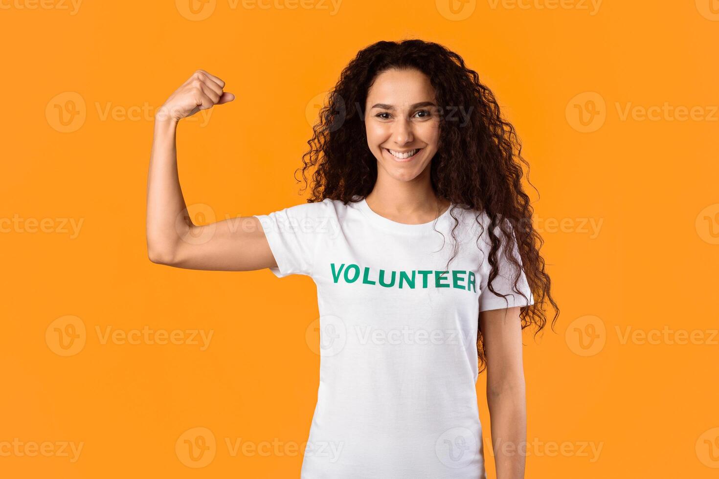 Power Of Kindness. Volunteer Lady Posing Showing Biceps Muscles Standing Over Yellow Studio Background, Smiling To Camera. Volunteering Missions, Charity And Voluntary Job Concept photo