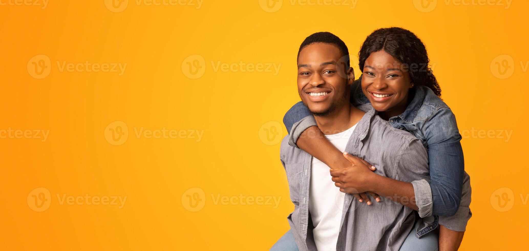 Cheerful Romantic Black Couple Having Fun Together, Loving African American Guy Piggybacking His Girlfriend, Cheerful Lovers Fooling Over Yellow Background, Enjoying Time With Each Other, Copy Space photo