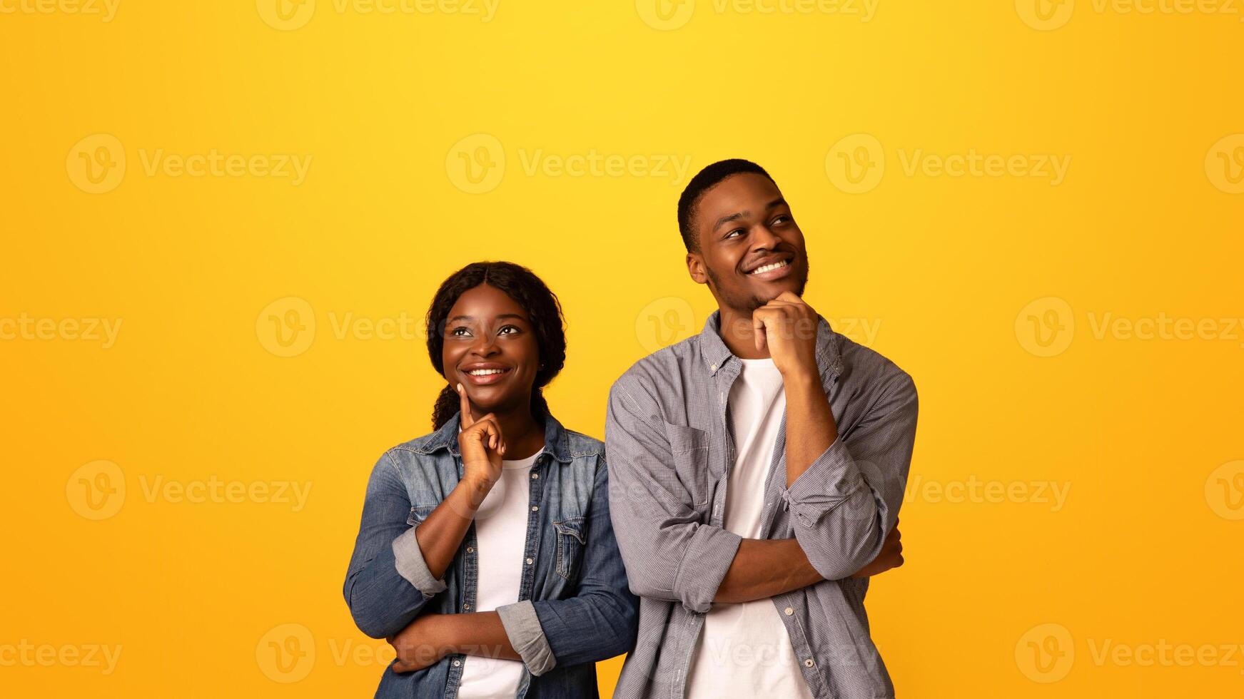 Dreamy young african american couple thinking about something and looking away, pensive black man and woman touching chins and smiling while standing isolated over yellow background, copy space photo