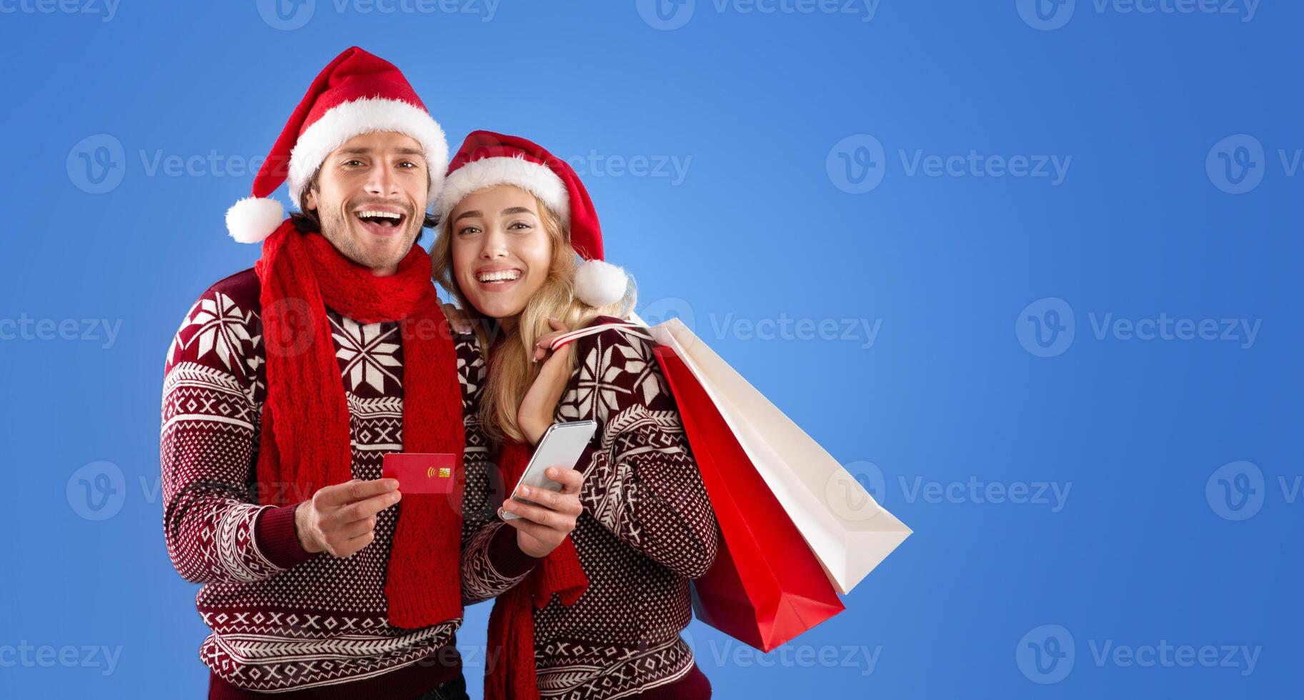 Romantic young couple shopping for Xmas gifts online with credit card and smartphone over blue background photo