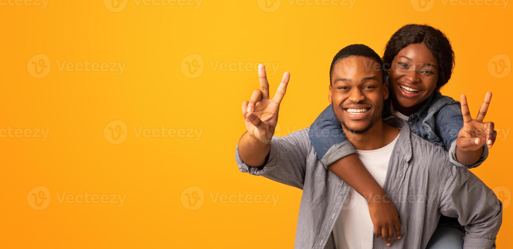 Portrait Of Cheerful Black Lovers Having Fun, Embracing And Showing Peace Gestures At Camera, Young Positive African American Couple Fooling Over Yellow Background, Enjoying Spending Time Together photo