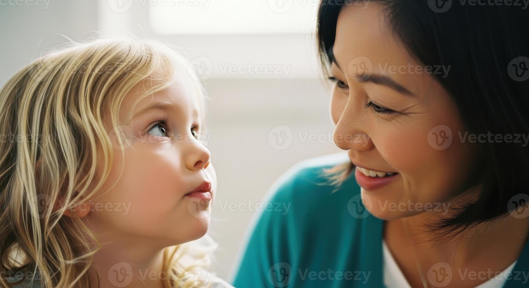 Curious blonde child looking up at smiling asian woman, fostering connection and learning photo