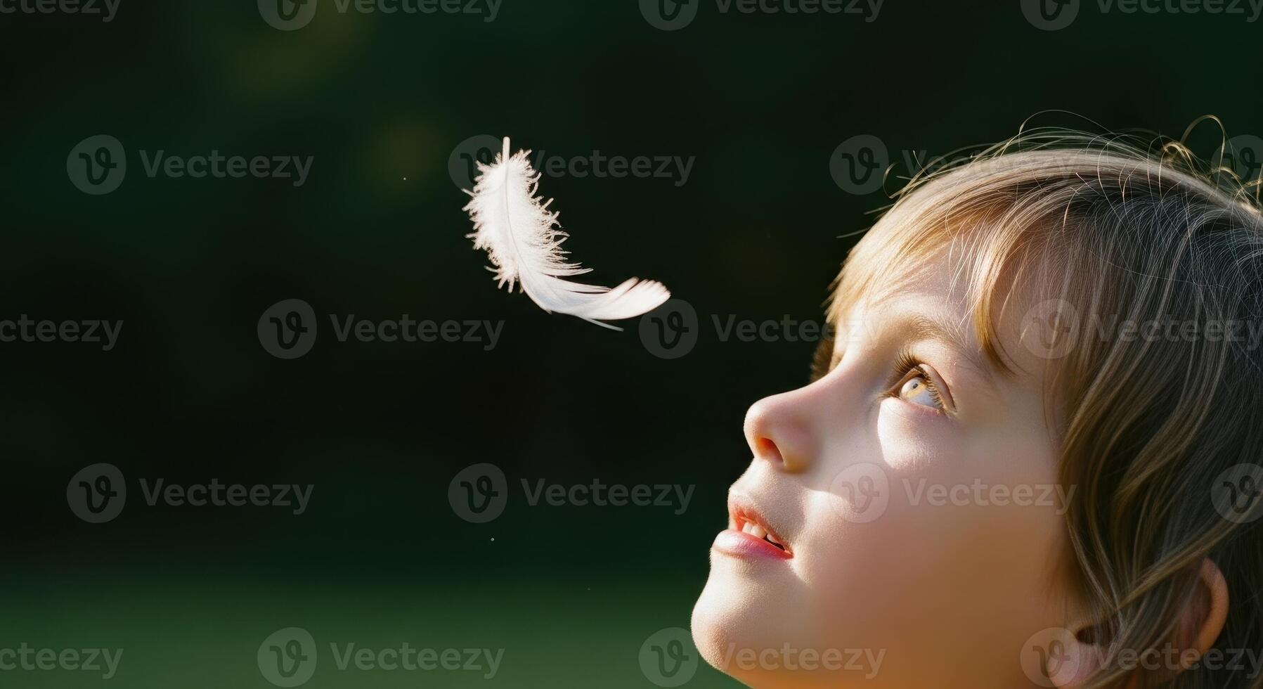 Young child looking up with innocent wonder at a delicate white feather floating in the air photo