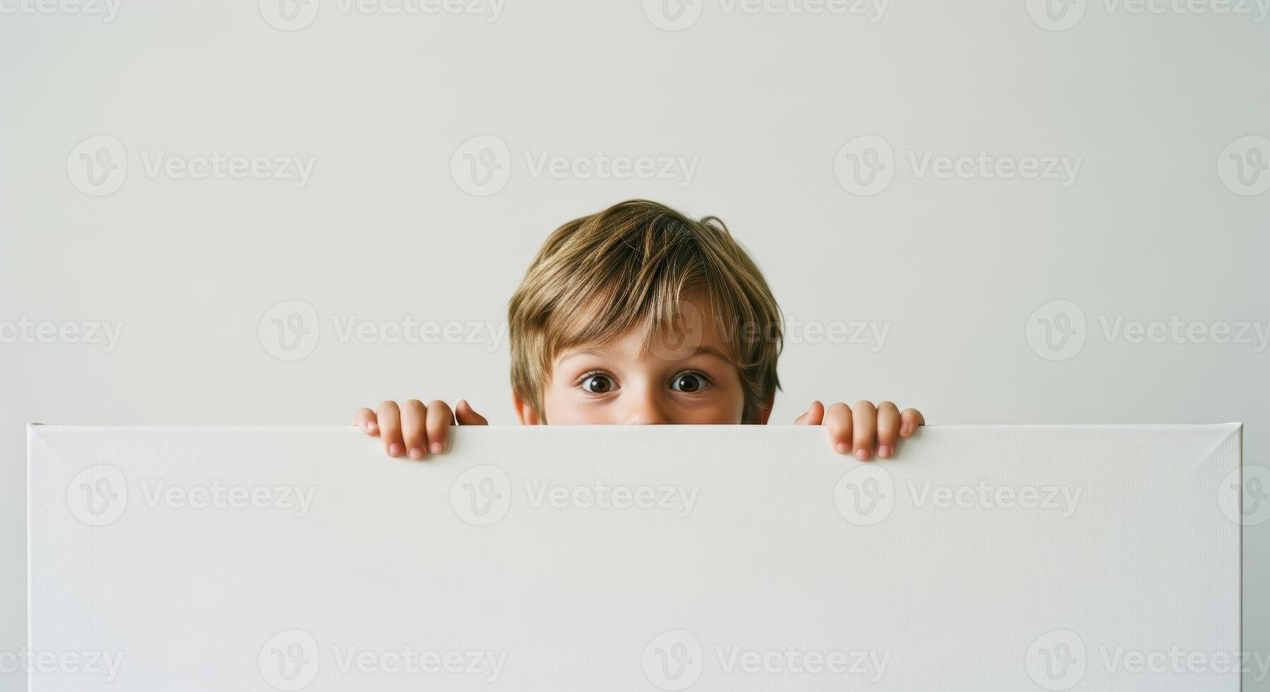 Curious little boy peeking over a blank white canvas with wide eyes photo
