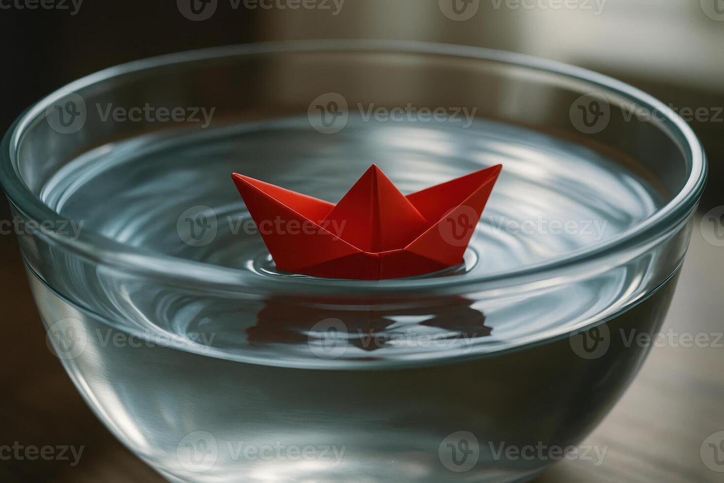 Bright red paper boat floating in clear glass bowl with rippling water photo