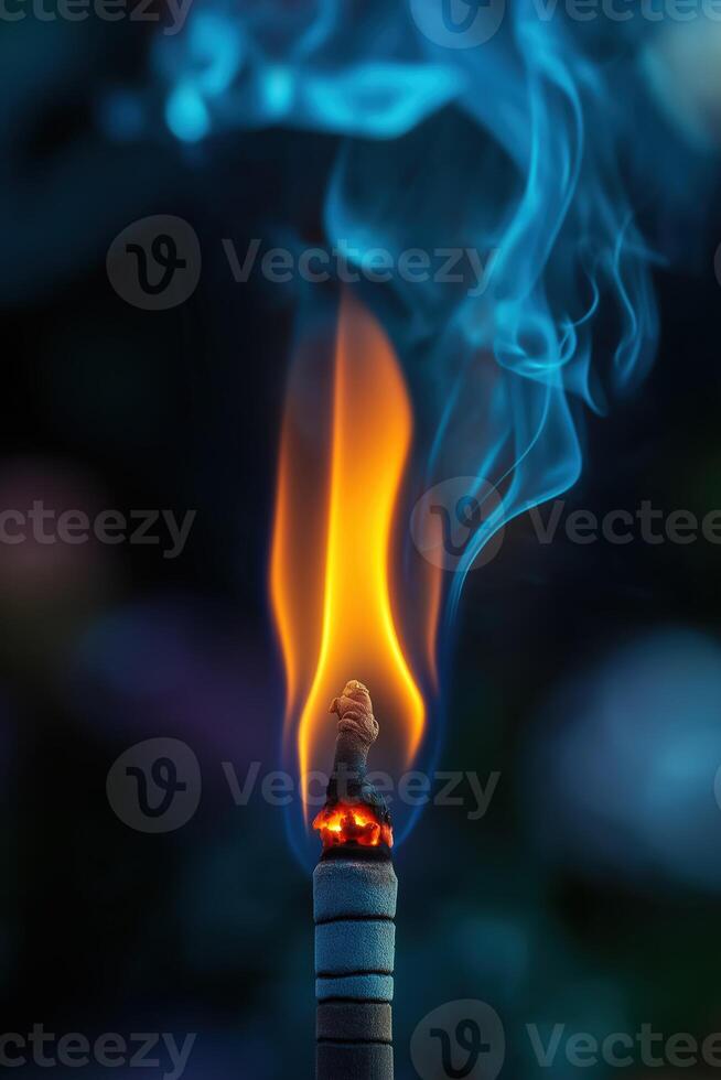 Burning incense stick with blue smoke and orange flame on dark background photo