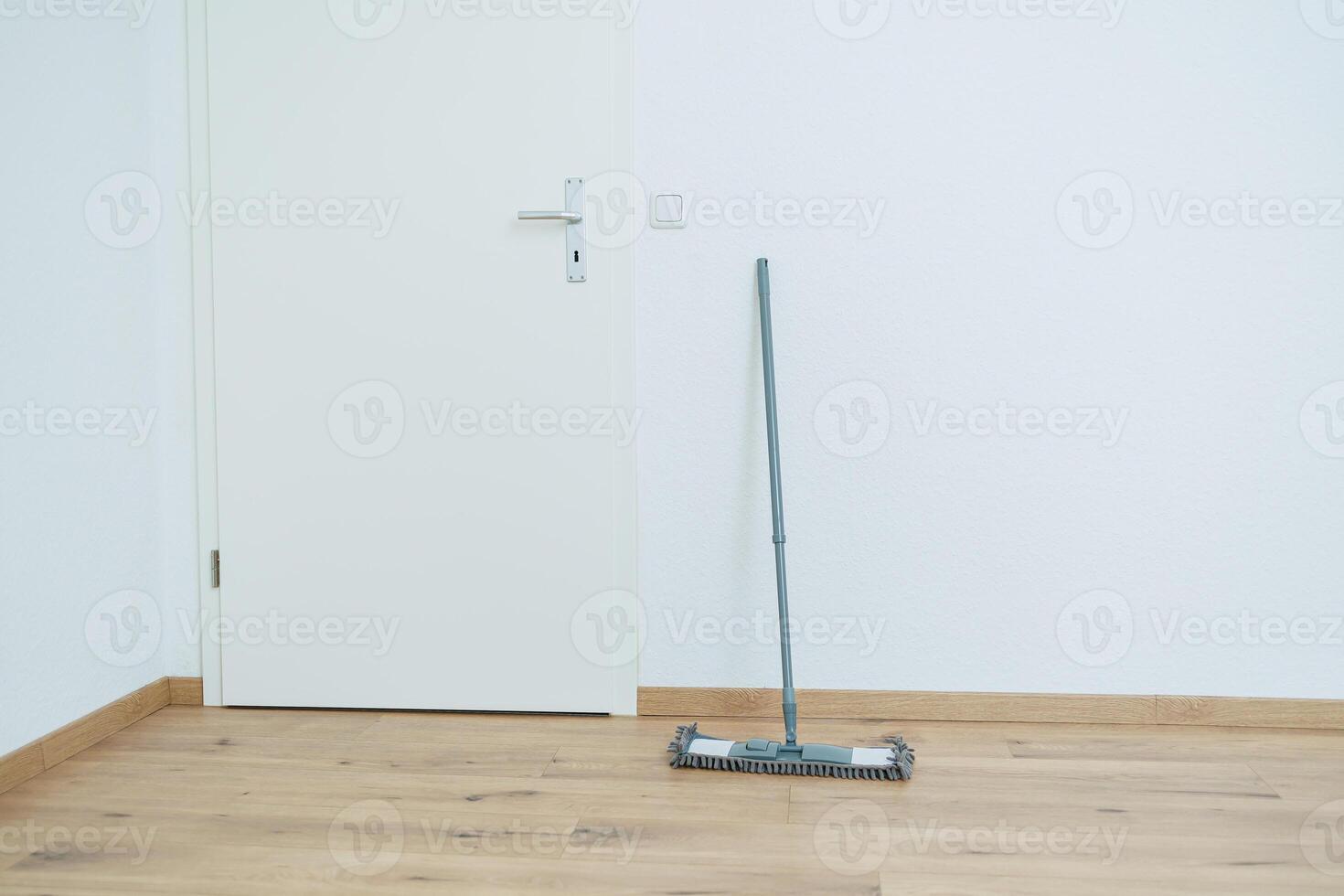 An empty room with a wooden door and a mop lying on the floor photo