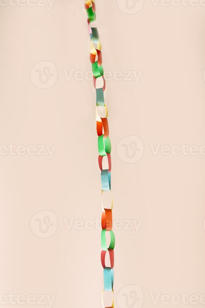 Vertical chain of interlinked colorful paper rings suspended against soft beige background. This vibrant handmade garland , childhood creativity, festive decor, crafting with simple materials photo