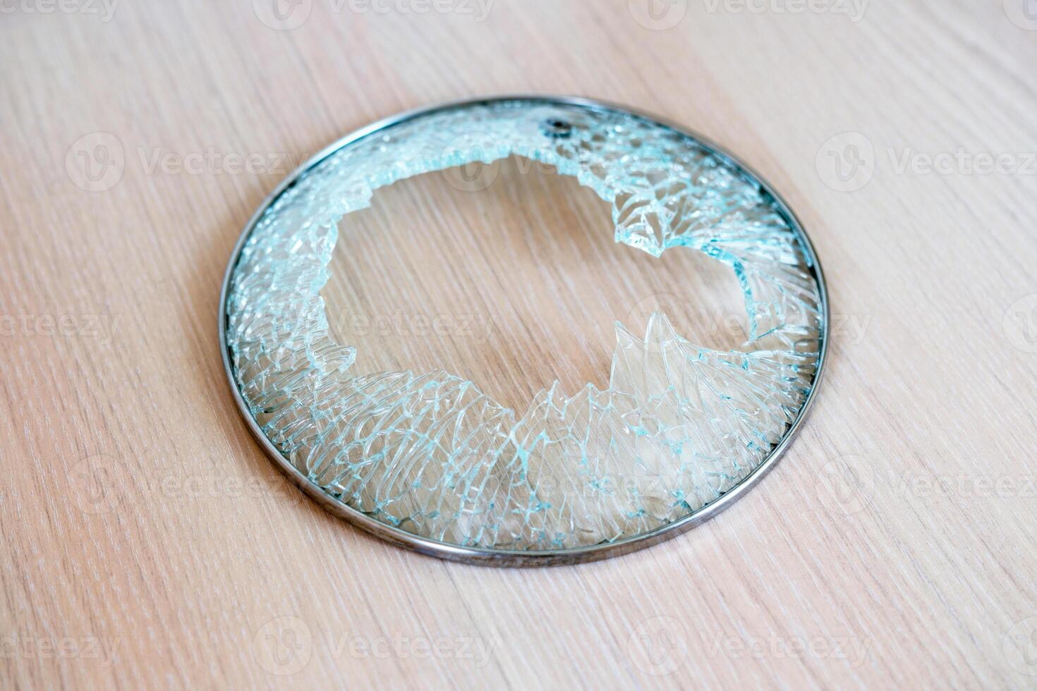 close-up shot of shattered glass circular lid with metal rim from cooking pot, resting on wooden surface, large central break with jagged, splintered edges, suddenness of an accident in kitchen photo