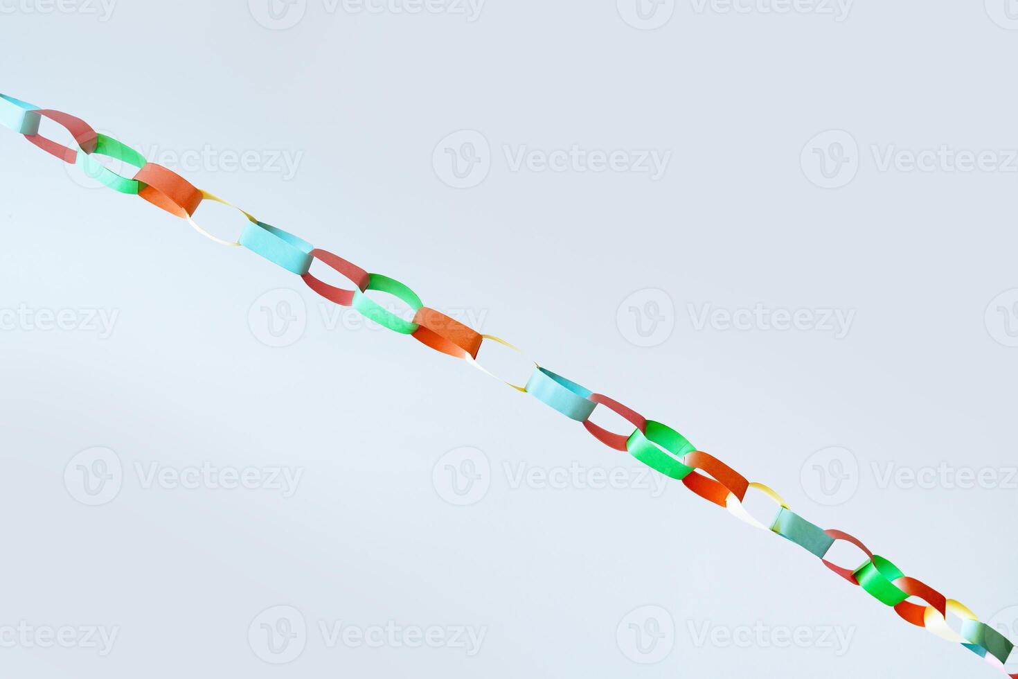 Diagonal view of multicolored paper chain garland hanging against white backdrop, fun and celebration, ideal for illustrating concepts of holidays, crafting, childhood activities, or decorative art photo