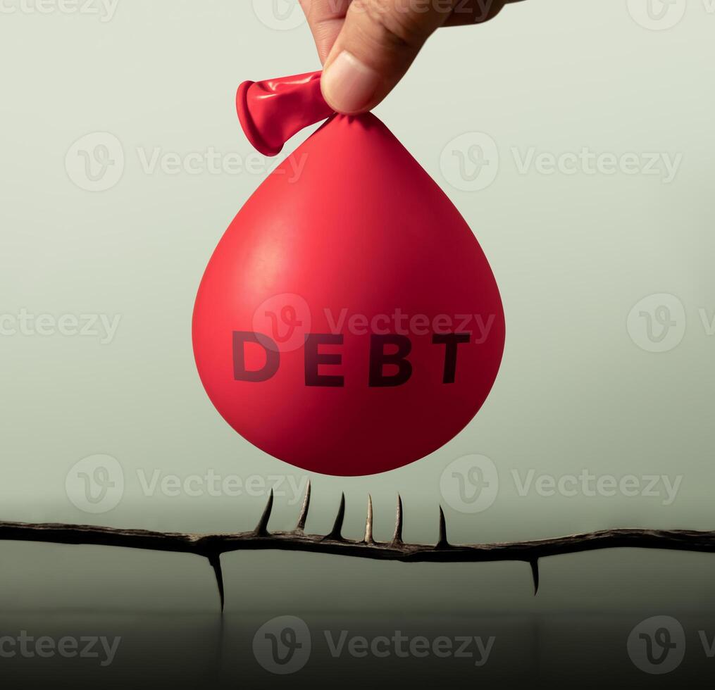 A water-filled balloon labeled DEBT hovers dangerously above spikes, symbolizing risk, debt crisis, financial instability and economic collapse photo