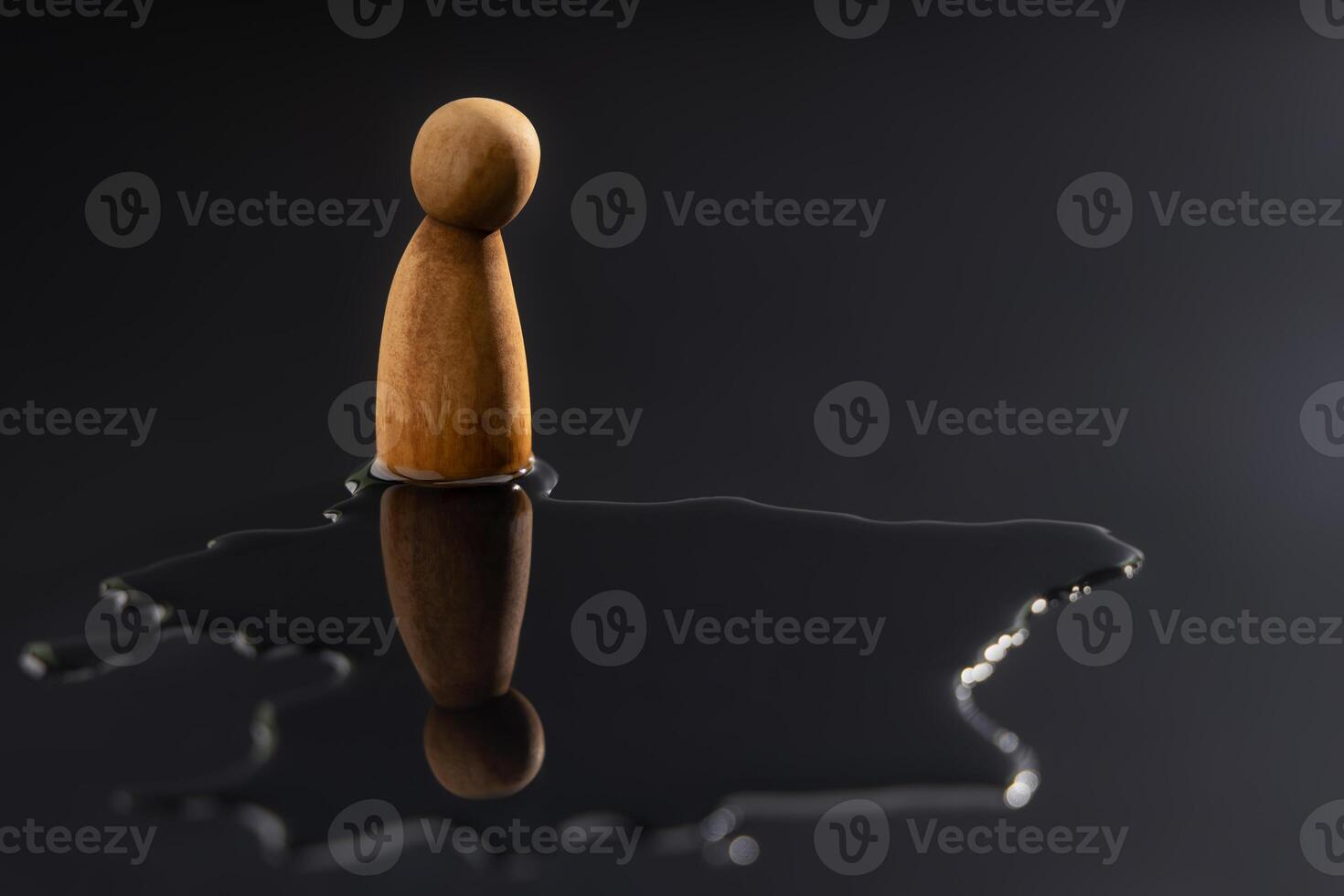 A wooden peg doll stands alone, staring down at its reflection in a puddle. Symbolizes symbolizing mental health crisis, deep depression, stress, and emotional pressure photo
