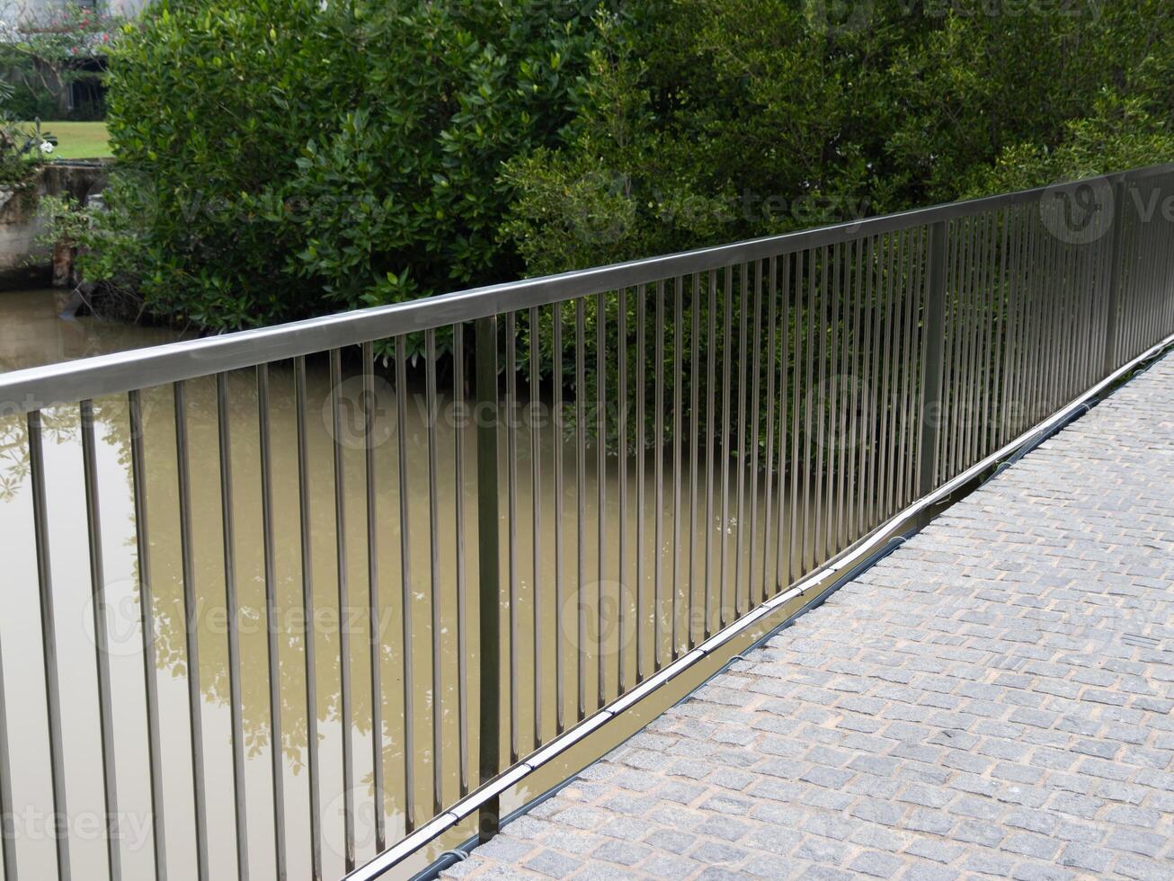 Calm urban park landscape metal fence with scenic view of murky water straight angle photo