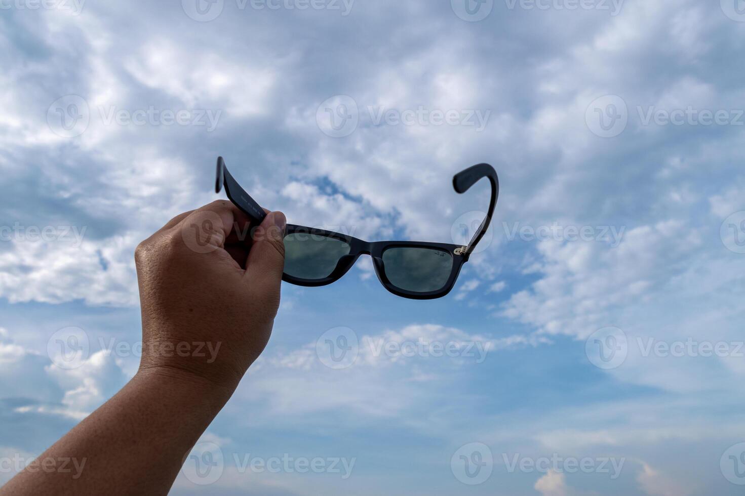 Holding sunglasses against dramatic sky outdoor scene perspective conceptual vision photo